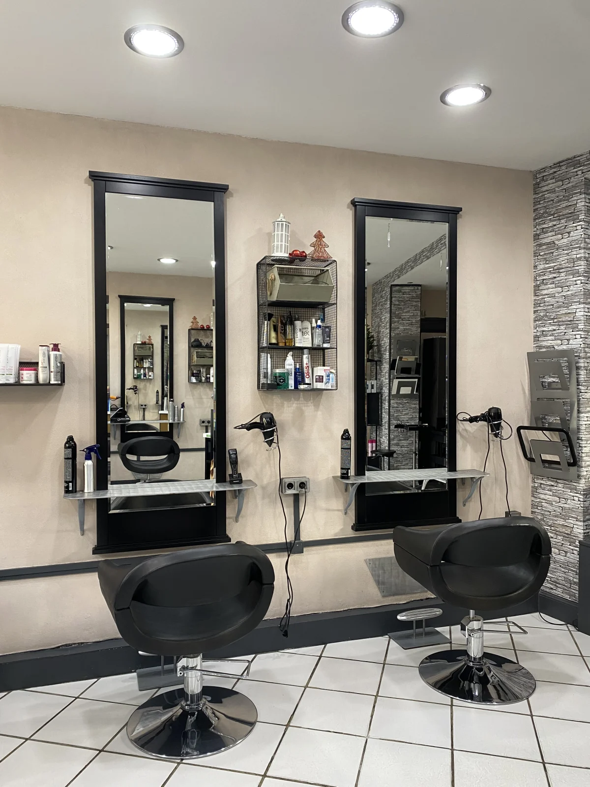 Deux postes de coiffage du salon, miroirs à cadre noir et fauteuils sur pied chromé